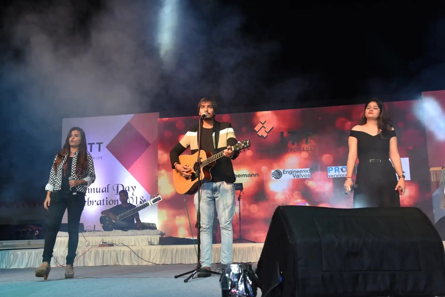 Musical performance on stage with three performers and ITT banner in background